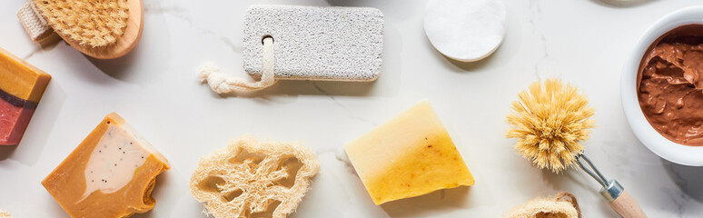 panoramic shot of loofah, pumice stone, body brushes, cotton pads and homemade soap on marble...