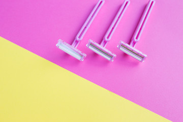 Three women's razors pink on an isolated pink and yellow background.