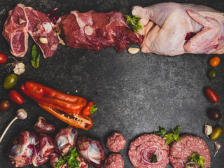 Different types of raw pork meat, beef, chicken, turkey giblets and tomatoes, garlic, bell pepper,greens. On the black concrete background. Copy space