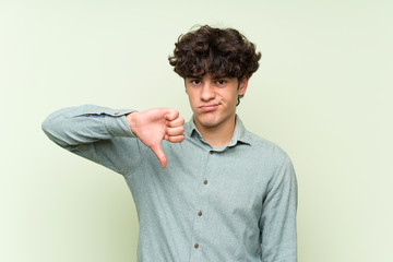 Young man over isolated green wall showing thumb down sign