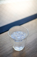 A cup of cold water on the wooden table with sunshine through the glass window