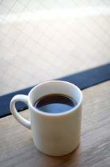 A cup of coffee on the wooden table with sunshine through the glass window