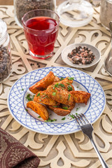 Baked unpeeled potato wedges on white plate and glass of red drink on oriental wooden table
