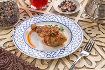 Grilled chicken legs with parsley on white plate and glass of red drink on oriental wooden table