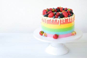 Cake on birthday with colorful rainbow cream on a white background decorated with berries, colorful sprinkles, poured with chocolate.