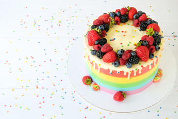 Cake on birthday with colorful rainbow cream on a white background decorated with berries, colorful sprinkles, poured with chocolate. Top view.