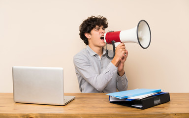 Young student man with a laptop shouting through a megaphone