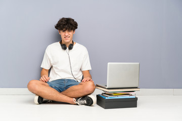 Young man with his laptop sitting one the floor having doubts and with confuse face expression