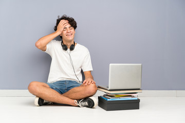 Young man with his laptop sitting one the floor laughing