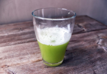 Green vegetable juice in glass on wooden background close up view