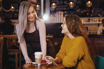 Young pretty woman and waitress in cafe.
