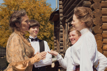 Historical reenactment. Men and women dressed 19th century clothes actively talk in the backyard of a wooden house. People relationships.