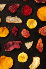 Dry fruit and vegetable chips, shot from above. Healthy vegan snack, an organic food flat lay pattern on a black background
