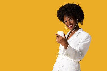 happy african american girl listening music while holding smartphone isolated on orange