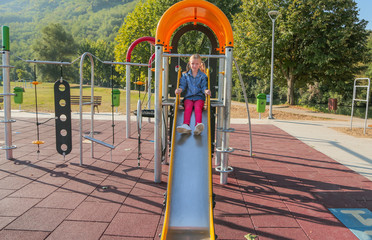 Little happy girl playing in children's slide in colorful modern playground for kids. 