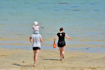 Un jeune couple qui coure avec leur enfant sur une plage en Bretagne