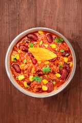Chili con carne, shot from the top on a dark rustic wooden background with a nacho and copyspace