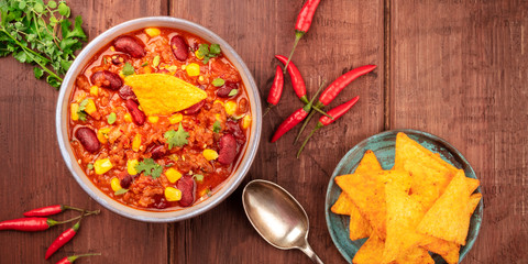 A panorama of Mexican food. Chili con carne, chilli peppers, cilantro leaves, and nachos, shot from the top on a dark rustic wooden background
