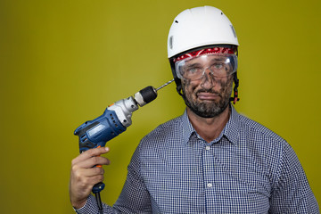 funny portrait of a stressed and depressed worker with helmet  putting the drill on his head