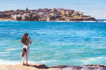 Poster Young woman using smartphone take photo landscape view of Bondi beach at sydney city, Australia. © sakarin14