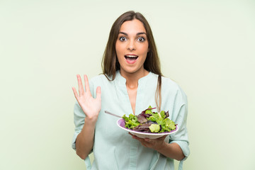 Young woman with salad over isolated green wall with shocked facial expression