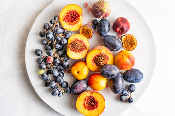 Naklejka na ściany i meble Halved peaches, nectarines, grapes, figs on white plate on white tablecloth.
