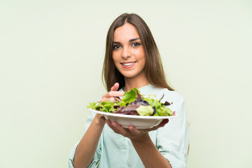 Young woman with salad over isolated green wall