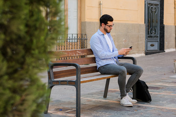 Young businessman is sitting on a bench while he is talking on the mobile