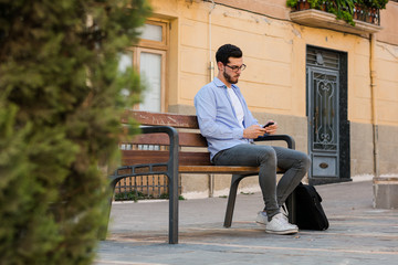 Young businessman is sitting on a bench while he is talking on the mobile