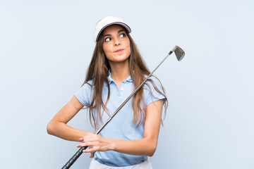 Young golfer woman over isolated blue wall looking up while smiling
