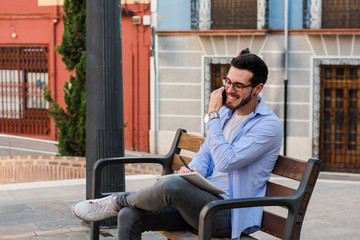 Young businessman is sitting on a bench while he is talking on the mobile and is writing in his notebook