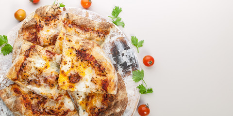 Slices Pizza Quattro formaggi on a round cutting board with cherry tomatoes and herbs. Copy space