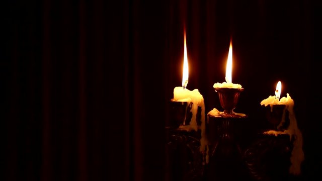 Three candles burn in a candlestick on a black background. Wind blowing on fire. Wax dripped from a burning candle.