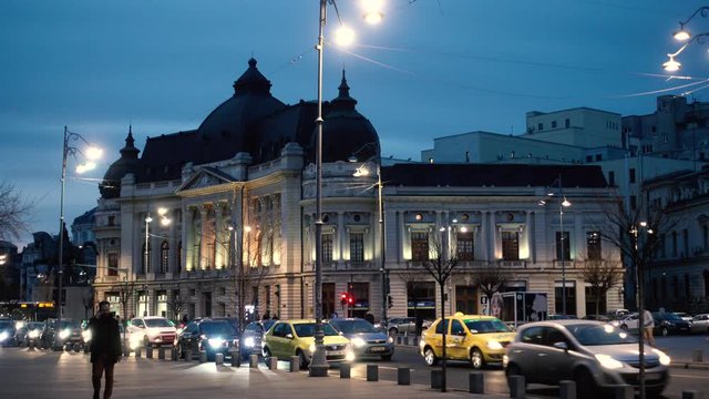 Bucharest, Romania - June 26, 2019 4k video Man walking down the Calea Victoriei at night and speaking o a mobile phone. Big traffic cars near the National Library and statue of King Carol I