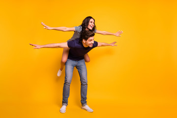 Fototapeta na wymiar Full length body size photo of cheerful friendly kind nice couple of two people wearing jeans denim playing airplane with each other while isolated with yellow background