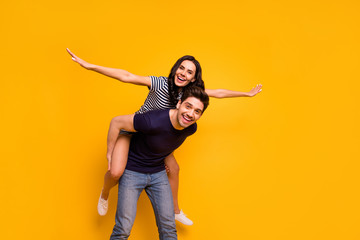 Fototapeta na wymiar Photo of cheerful crazy couple of friends with girl pretending to be airplane and guy holding her on back while isolated with yellow background