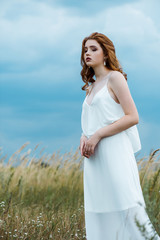 Fototapeta na wymiar upset and pretty young woman in dress standing in field