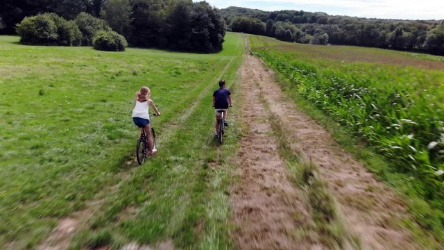 un couple qui fait du v&eacute;lo dans la campagne au milieu des champs et d'une for&ecirc;t