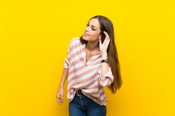 Young woman over isolated yellow background listening to something by putting hand on the ear