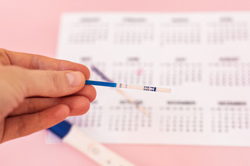 Fototapeta premium Beautiful female hand with red fingernails holding positive pregnancy test isolated on pink background. Motherhood, pregnancy, birth control concept. Minimal sparse modern image language.