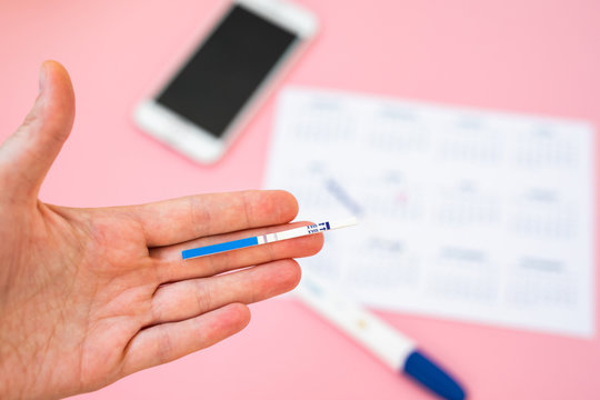 Beautiful female hand with red fingernails holding positive pregnancy test isolated on pink background. Motherhood, pregnancy, birth control concept. Minimal sparse modern image language.