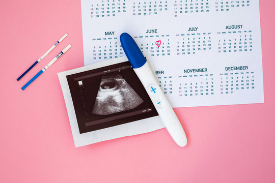 Ultrasound photo and pregnancy test on pink wooden background