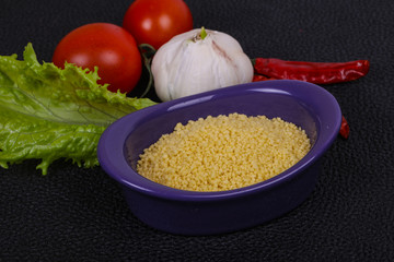Raw couscous in the bowl served salad leaves, tomato and pepper