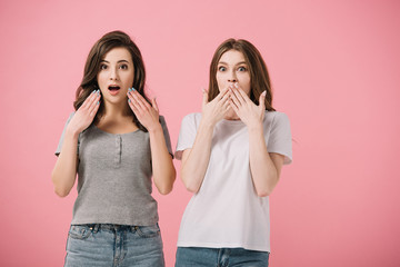 attractive and shocked women in t-shirts looking at camera isolated on pink