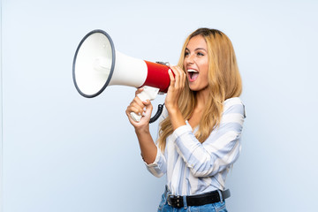 Young blonde woman over isolated blue background shouting through a megaphone