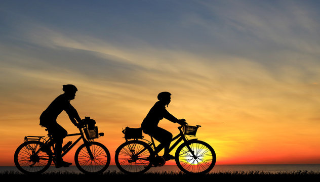 Silhouette couple and bike relaxing on blurry sunset background.