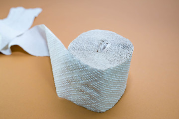 Rough toilet paper role fabricated from recycled paper on brown surface .