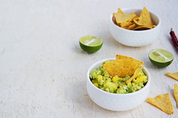 Appetizer, guacamole with mango in a white bowl on a light concrete background. Served with corn chips nachos. Mexican cuisine. Copy space.