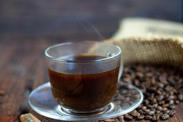 Coffee in a transparent cup. Hot, invigorating drink. Near cones in sparkles, coffee beans are scattered.