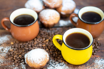 Coffee in brown cups. Hot, invigorating drink. Coffee beans are scattered nearby. In the background homemade cupcakes. 